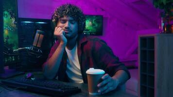 Tired sleepy Indian American man yawning male guy player playing game influencer broadcast drink coffee computer addiction exhaustion cyber gaming streamer hacker night insomnia yawn programmer video