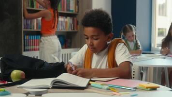 African American little boy child guy schoolboy pupil kid son primary elementary education student school lesson end writing in copybook studying learning at desk prepare study learn books in library video