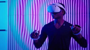 Smiling happy African American man in VR glasses play virtual reality game in neon futuristic space browsing interactive future software interface guy male cyberpunk innovate simulation helmet working video