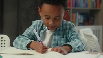 Cute little boy kid child African American son schoolboy elementary primary education studying in school write draw notebook at desk classroom lesson writing homework study learn pupil student library video