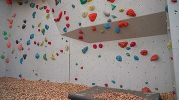 Climbing artificial rock climbing wall to practice mountain bouldering and climbing skills with colored grips and route markers for beginners. Bouldering track on simulated rock boulder walls. video