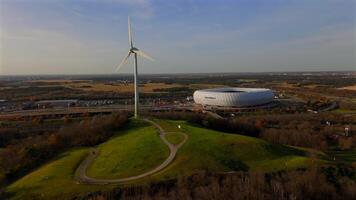Aerial view of the Froettmaninger Hill with a wind turbine and a scenic view of the Allianz Arena in Munich. Freimann wind power plant and Munich football arena captured from above. video