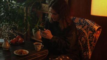 Young woman using smartphone during tea break in cozy living room. Person enjoying free time at home, drinking hot tea. video