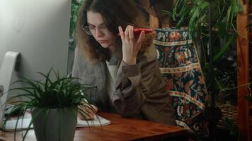 Remote work in home office. Female freelance employee listens to audio file, voice message on smartphone sitting at her workplace. video