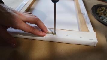 Stretching canvas on stretcher. Close-up of hands screwing fasteners to picture's stretcher with screwdriver. video