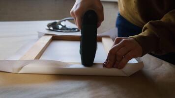 Framer hands stretching canvas on wooden stretcher frame using staple gun. video