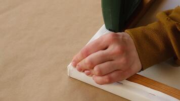 Canvas stretching. Hands staple canvas onto wooden stretcher using staple gun. Gallery wrap, canvas print. video