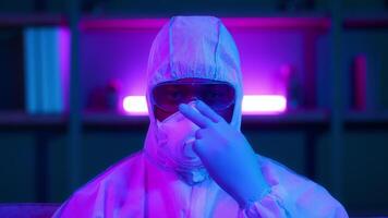 An African American man wears a protective suit and mask while working in a modern environment illuminated by vibrant neon lights, emphasizing the urgency of pandemic safety measures. video