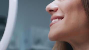A young woman is smiling while sitting in a dental chair. The dentist is preparing for a routine check-up, ensuring a comfortable environment. The clinic features a clean and modern design, cropped video