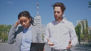 A businessman and businesswoman engaged in a discussion outdoors, analyzing data on a tablet. They represent a diverse group of millennials collaborating in a corporate environment. video