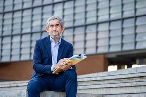 Portrait of confidence senior asian CEO businessman is sitting and holding document and digital tablet at his modern office for market leader, manager, executive corporate and millionaire photo