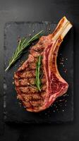 Juicy steak grilled on the bone with spices and herbs on a black stone background top view free copy space photo