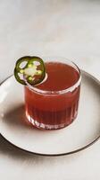 A drink with a green jalapeno garnish on a white plate photo