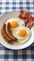 A plate with eggs, bacon and sausage on a checkered tablecloth photo