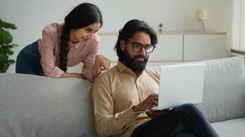 Arabian Indian couple on couch sofa use computer laptop shopping online internet store happy multiracial wife husband smiling lovely customers woman and man search goods purchase on website at home photo