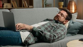 Lazy relaxing lying on sofa couch Caucasian man male freelancer businessman business guy online shopping order food delivery laptop computer working pc browsing net playing internet game web at home photo