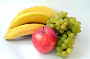 Big red apple in front of the bunch of bananas and ripe indian green grape isolated on white background photo