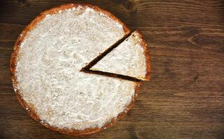 Slice of homemade pie with lemon and orange filling, covered with powdered sugar on a wooden table. copy space photo