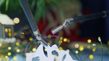 Tiny claws of the robotic arms tying the thread to the paper snowflake. Precise movements of the equipment. Christmas decorations at the backdrop. video