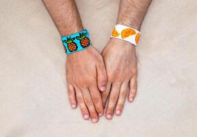 Males hands with woven friendship bracelets with alpha pattern pineapples and oranges fruit handmade of thread on beige background photo