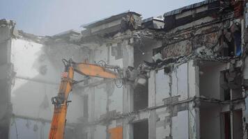 A scoop of demolishing machine breaks off the floors of the destroyed house. Excavator working in the cloud of dust . video
