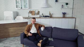 Man using smartphone at home. Young man sitting on sofa, using mobile phone video