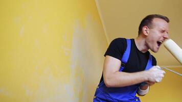 Man singing in paint brush. Cheerful man with rollers for painting the walls singing video