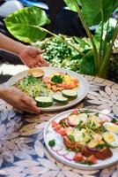 waitress holding a plate with eggs bennedict waffles with smoked salmon and serving on a table with chicken toasts in restaurant photo
