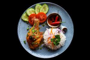 Roasted chicken leg in a Vietnamese style with rice, vegetables and sauce isolated on black background top view photo