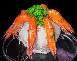 Five orange shrimp inside of coconut with sauce isolated on black background top view photo