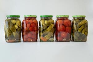 several glass jars of canned cucumbers, gherkins and tomatoes photo