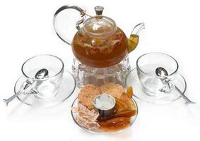 Glass tea pot with cups and crystalized fruits on white background photo