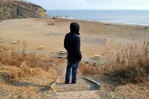 Upset man standing in black jacket on destroyed stairs and looking at Japanese sea on an autumn day photo