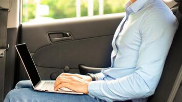 Handsome arabic guy in formal outfit entrepreneur sitting at auto back seat, using laptop with blank screen, typing on keyboard, sending emails while going to business meeting, mockup, copy space photo