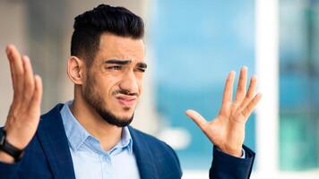 Closeup portrait of furious middle eastern young man businessman gesturing, expressing negative emotions, having crisis at job, experiencing difficulties at office, copy space photo