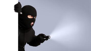 Disguised thief with robbery mask holding a flashlight behind a white panel isolated on gray studio background photo