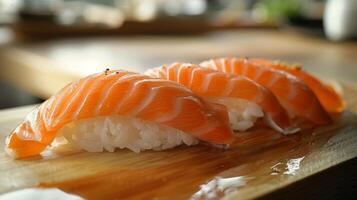 Three pieces of salmon sushi are artfully placed on a polished wooden platter, with their vibrant orange color complementing the white rice beneath. The setting has a warm, inviting ambiance. photo