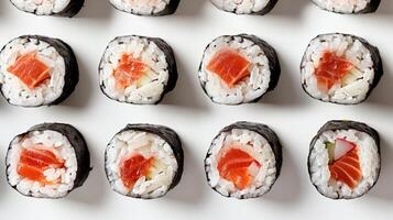 Fresh sushi rolls are displayed in an organized pattern on a white plate, featuring a mix of fish, rice, and vegetables, highlighting their vibrant colors and appealing presentation. photo