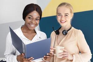 Happy female service desk consultants having coffee break at modern open space office, free space. Helpline operators with documents and hot drink smiling and looking at camera in call centre photo