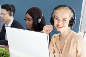 Multinational team of call centre operators speaking to customers online at modern office. Helpline consultants working in telemarketing or technical support, indoors photo