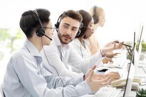 Male tech support operators communicating to solve client's request at call centre. Friendly young helpline consultants talking to each other at workplace. Hotline service concept photo