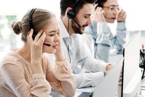Busy call center assistants with headsets working in front of computer monitors in open space office photo