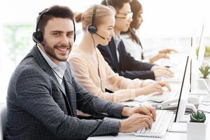 Team of customer service agents with headsets working at computers in office, copy space photo