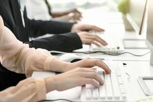 Cropped view of customer support operators at work in modern call centre, copy space. Team of young hotline consultants using computers at open space office, closeup of hands photo