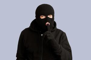 Don't Tell Anybody. Headshot of sneaky looter showing silence gesture, isolated over white studio background photo