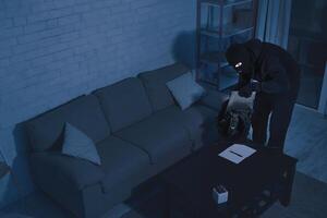 Security Camera Concept. Disguised thief stealing pc, putting it in his backpack in the night, high angle top view photo