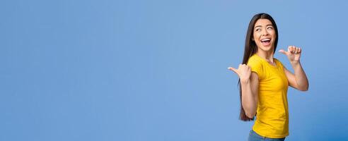 Best Choice. Joyful asian girl pointing on copy space behind her back with thumb ups, purple background, panorama photo
