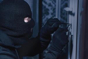 Vandalism Concept. Side view closeup portrait of unrecognizable thief in black balaclava unlocking door with picklock photo