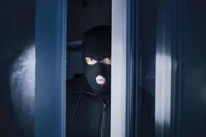 Burglary Concept. Evil thief looking at camera through open front door, entering enclosed property photo