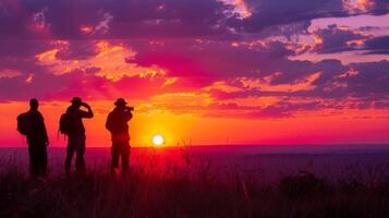 Silhouetted figures stand on a high vantage point, capturing the vibrant hues of the sky as the sun sets over the horizon during twilight. photo